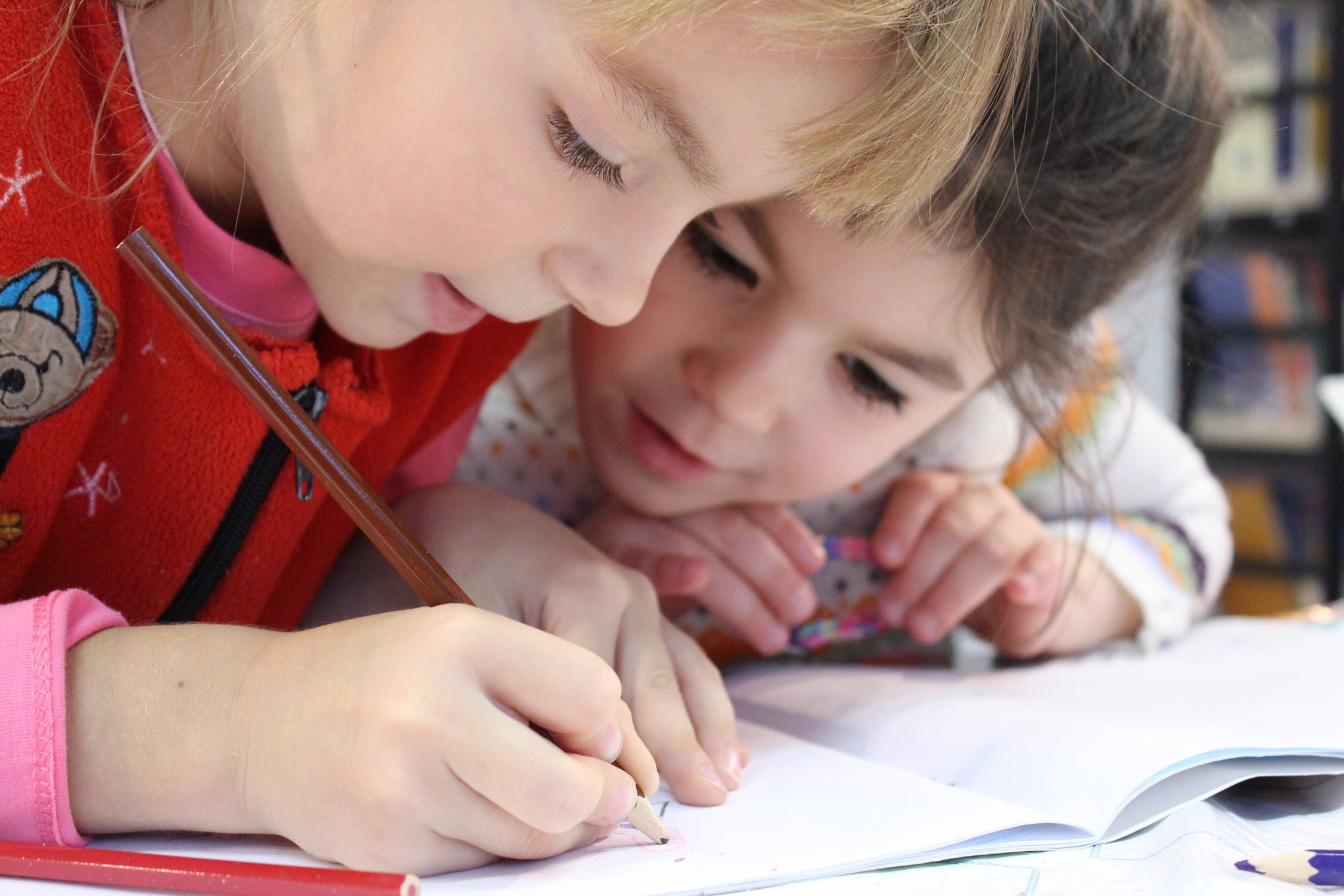 Image of school readiness: two young girls writing in an exercise book, heads close together looking happy
